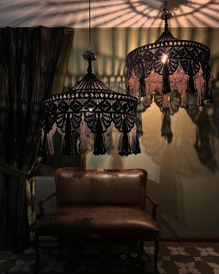 Black and blush macrame chandelier in a moody sitting room from @macramespb. Layered tassels cast patterned shadows.