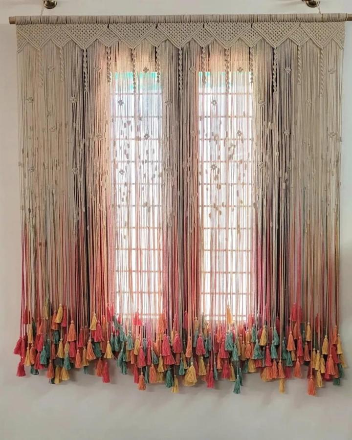 Neutral and jewel-toned macrame window curtain from @threadz.bar. Layered tassels soften two bright windows.