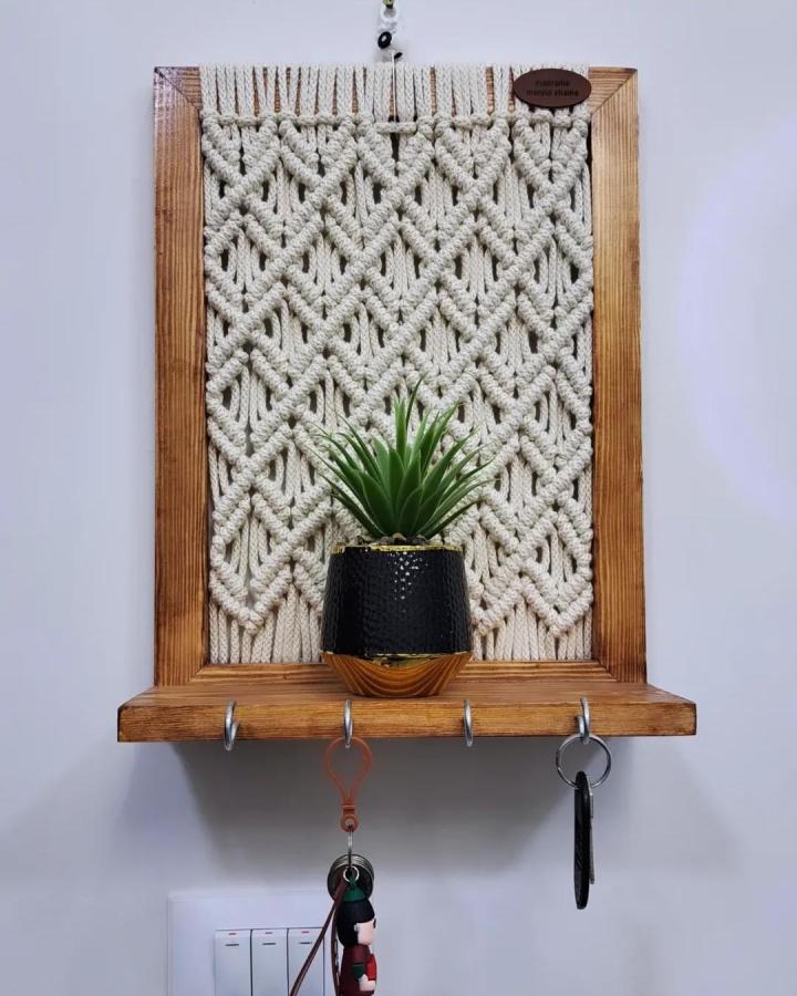 Cream macrame key holder from @mena_shams. Wooden frame, leafy plant, and hanging keys create a useful entryway accent.