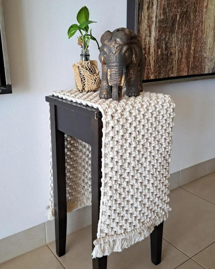 Cream chunky macrame console runner from @habubus_mx. Fringed textile layers a black table beside an elephant sculpture.