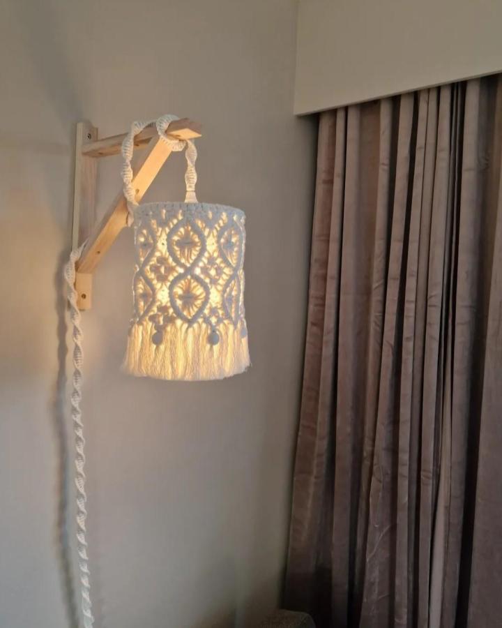 Cream macrame pendant lamp from @bare_linn. Woven hearts and fringe cast a warm glow beside taupe curtains.