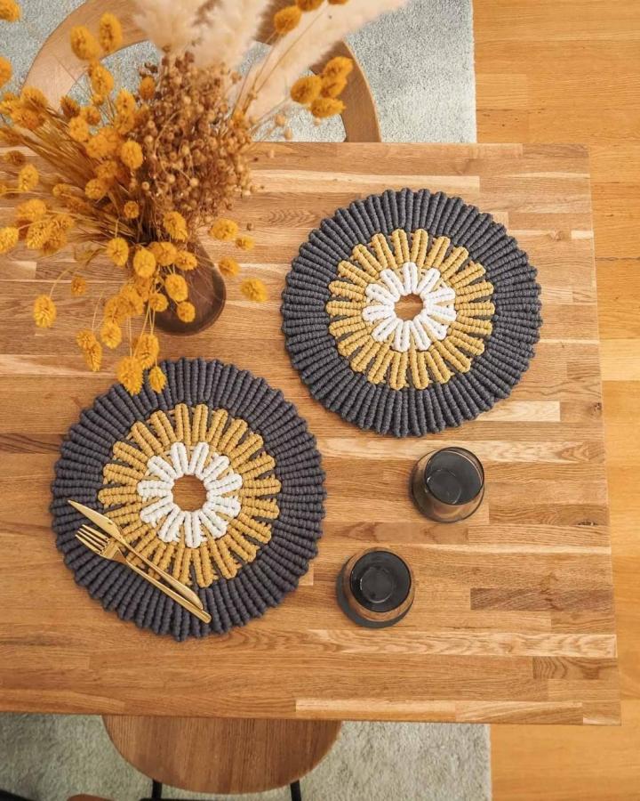 Charcoal, mustard, and cream round macrame decor ideas placemats from @macramemakersclub. Textured sunburst design on a wooden table.