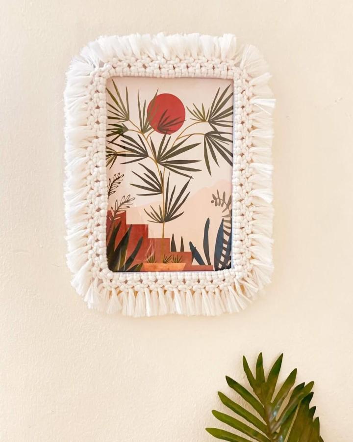 Ivory macrame wall frame from @salmaelsayeddesigns. Tropical print with fringe and botanical details.