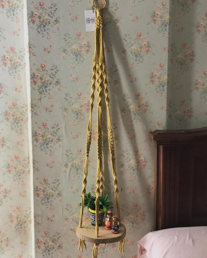 Mustard Yellow Macrame Hanging Shelf from @handmadewithlove_xoxo. Round wood perch holds a leafy plant and tiny figurines.