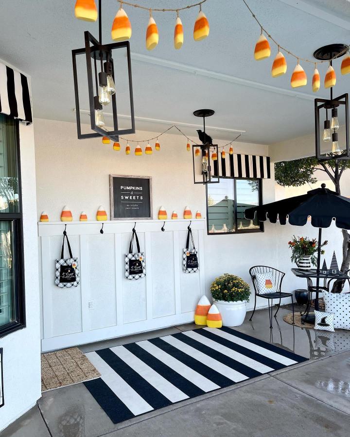 Orange, white, and black candy-corn porch display from @devanie.at.home. outdoor fall decor ideas with lanterns, garland, and striped rug.