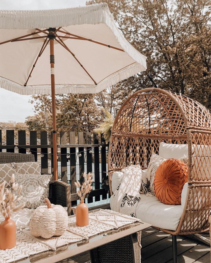 Cream rattan patio seating from @cassandra_corabi. Rust-orange pumpkin accents create a cozy autumn outdoor nook.