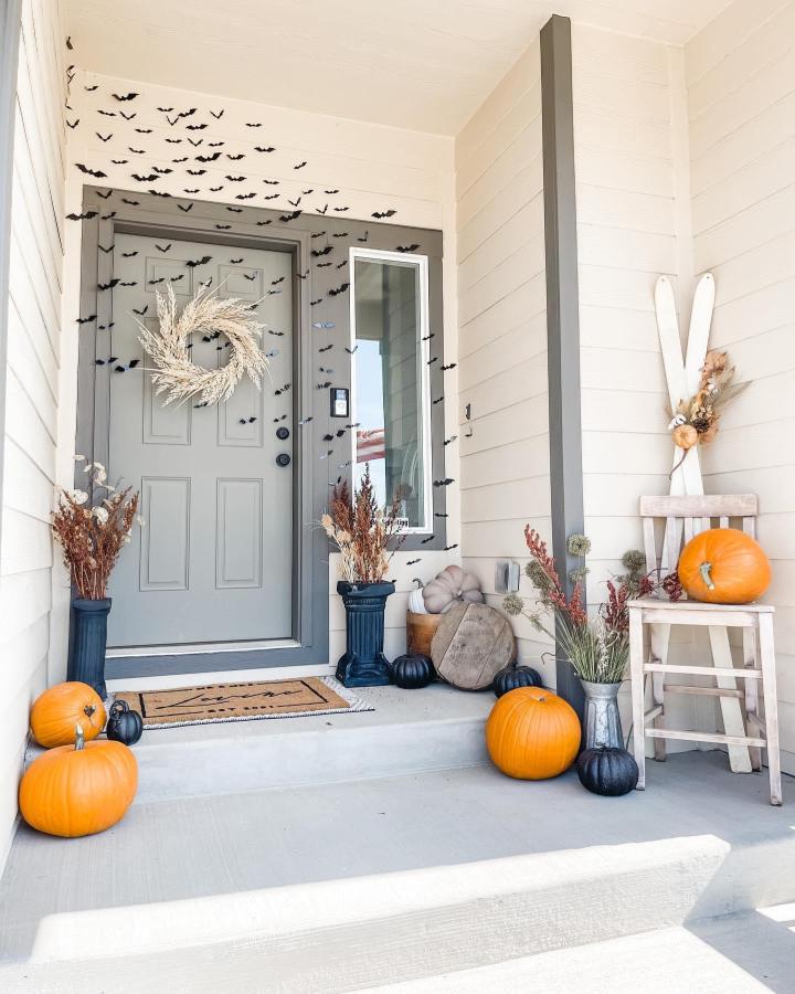 Black-and-orange porch from @byjamiemichelle. Outdoor fall decor ideas with bats, pumpkins, wreath, and dried botanicals.