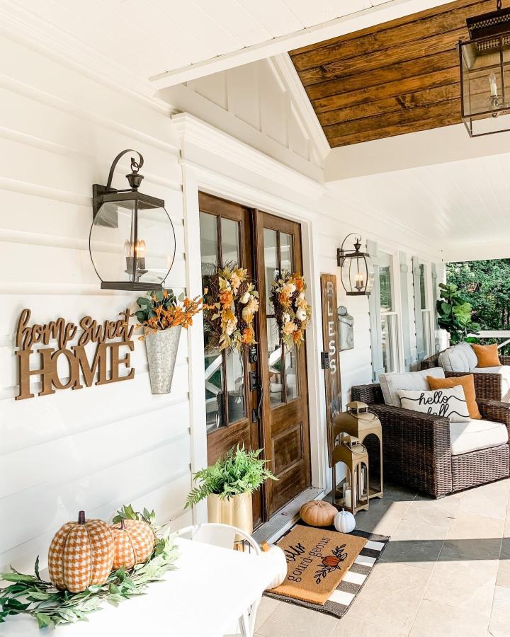 Warm white farmhouse porch from @ashleymariesavage. Amber wreaths, pumpkins, lanterns, and cozy autumn seating.