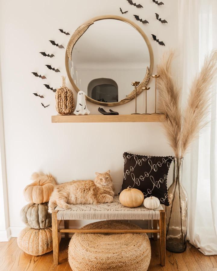 Neutral bat-themed entry vignette from @emilywelchstyle. Outdoor fall decor ideas feature pumpkins, pampas grass, and gold mirror.