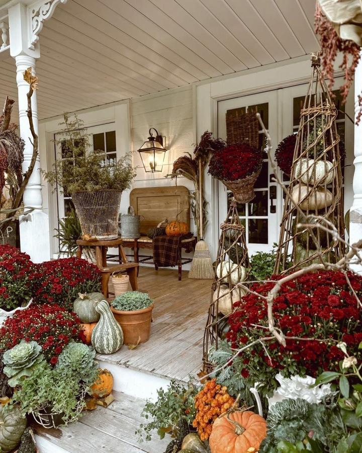 Red chrysanthemum porch display from @jensjunk. Layered pumpkins, pale green gourds, wicker baskets, and twig towers create autumn charm.