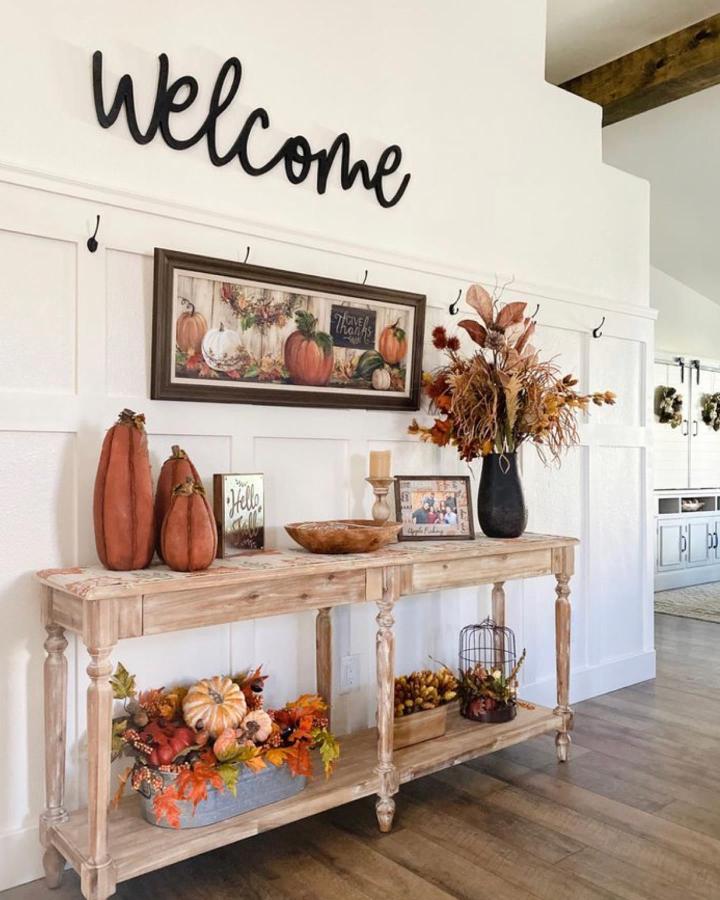 Rustic wood entryway console from @dreamhomesandlifestyle. Pumpkins, autumn florals, and framed harvest art create welcoming seasonal styling.