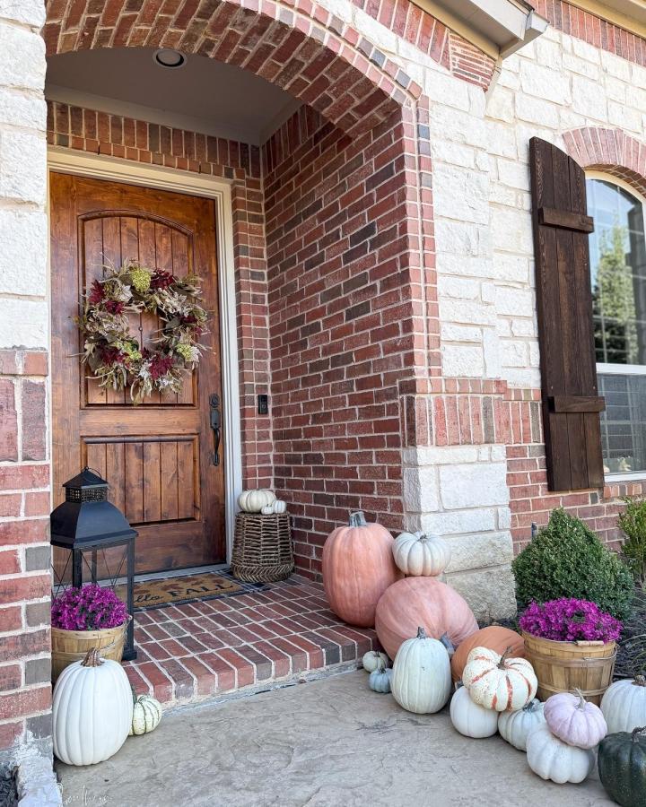 Muted fall brick entry from @southernhomeandhospitalityblog. Wreath, lantern, pumpkins, and magenta mums welcome guests.