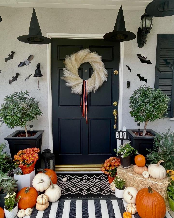 Cream pampas wreath front door from @poppyjameshomedesigns. Compact Halloween porch with pumpkins, bats, and witch hats.