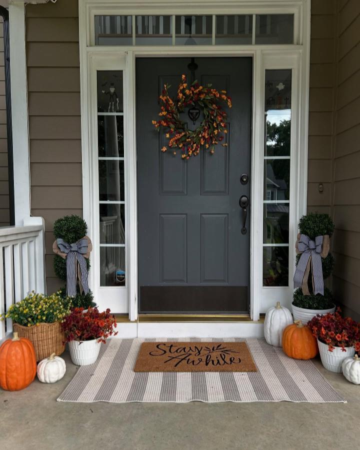 Autumn charcoal-gray porch from @haywoodhomedesign. A leafy wreath, pumpkins, striped bows, and layered rugs frame the entry.
