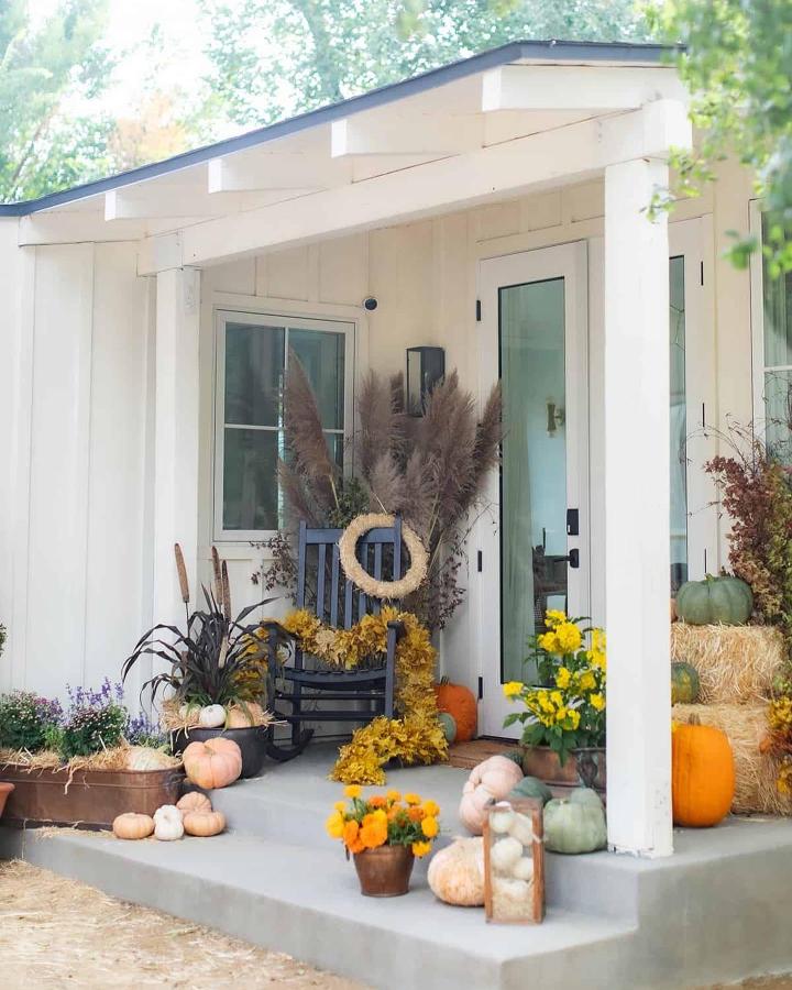 Warm autumn porch display from @sugarandcharm. Pampas grass, pumpkins, mums, and a wreath brighten the entry.