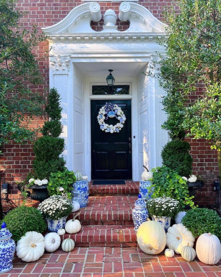 White pumpkins and blue ceramic planters from @meredithlewis05. Small fall porch decor ideas with topiaries and white mums.