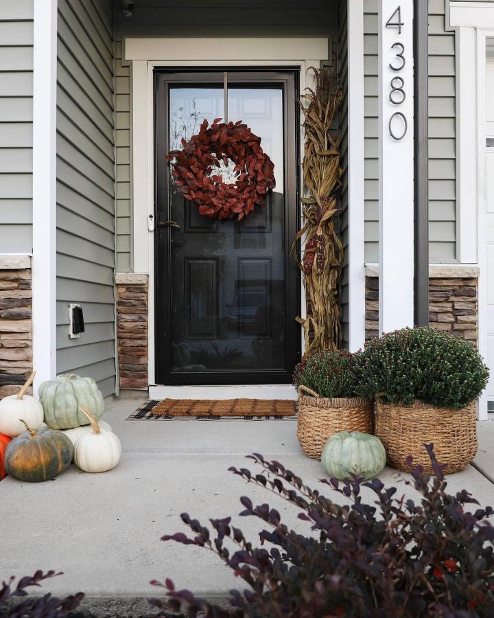 Burgundy wreath and woven baskets from @prettyrealblog. Compact porch with pumpkins, mums, and cornstalks.