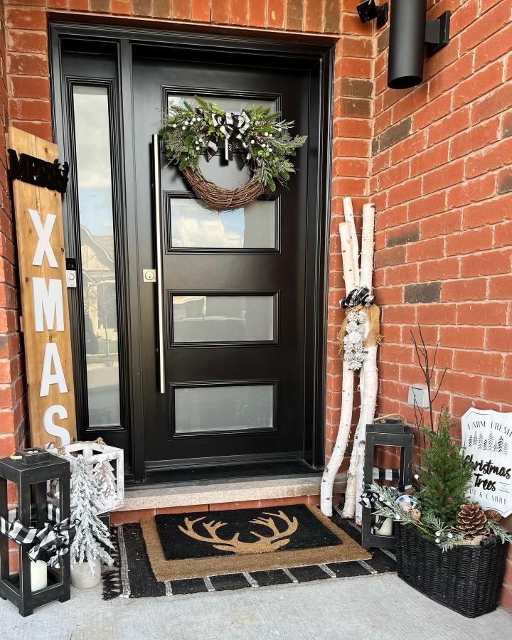Black-and-white fall porch entry from @cilthestager. Wreath, birch logs, lanterns, and layered mats.