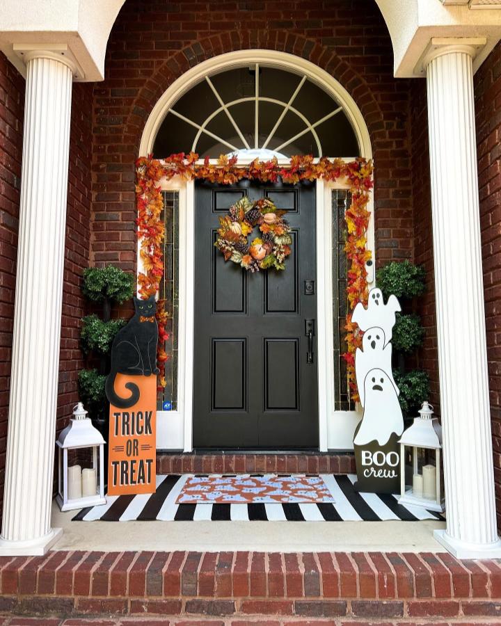 Autumnal black front porch from @savillamountain. small fall porch decor ideas with ghosts, pumpkins, garland, and striped mat.