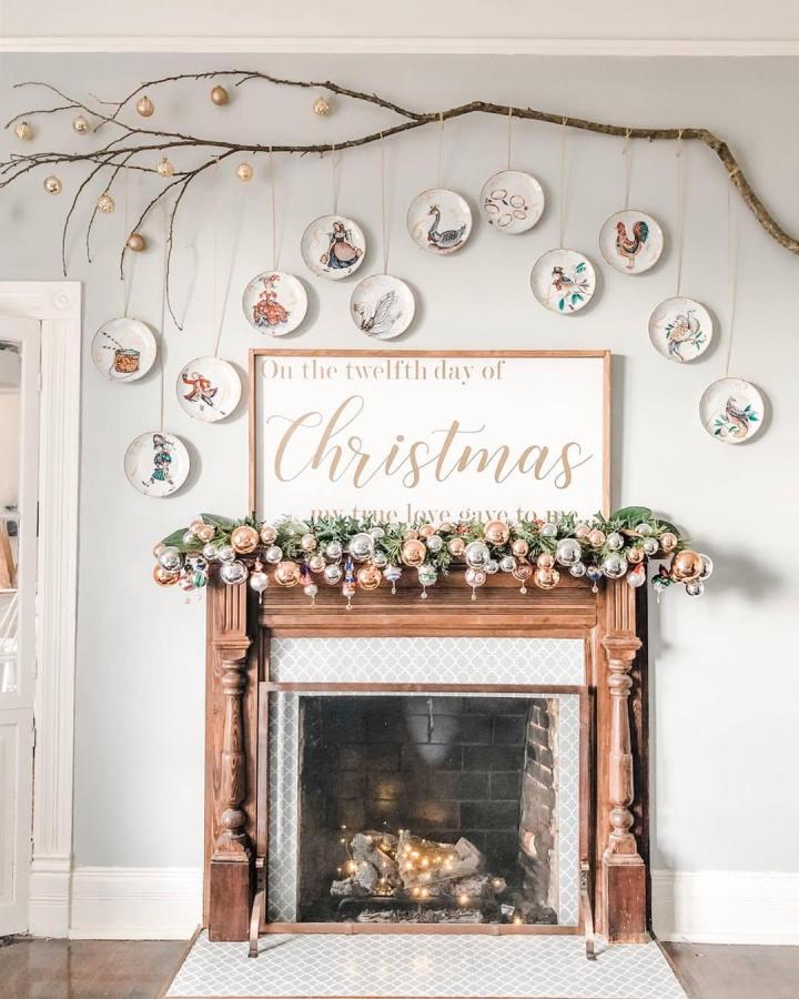 Natural brown branch mantel display from @katherinebrookscentral. White plates, metallic ornaments, and evergreen garland decorate a Christmas fireplace.