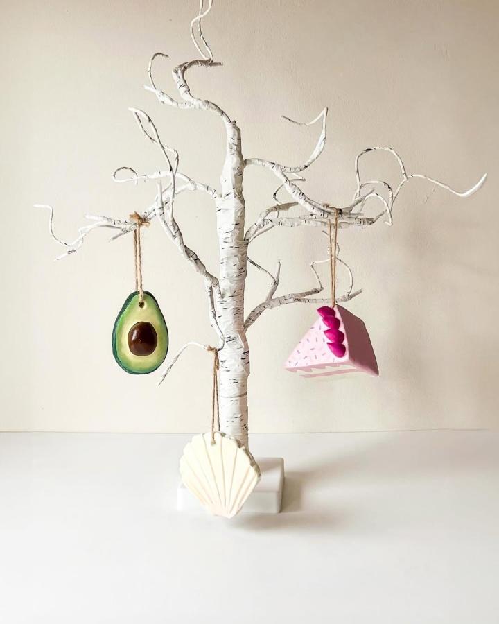 White birch branch ornament tree from @sculpdit. Colorful avocado, pink paper, and shell charms hang from curling twigs.