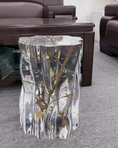 Clear resin tree branch stool table from @lumierecreation_ca. Reflective silver ripples encase twisting brown branches in a living room.
