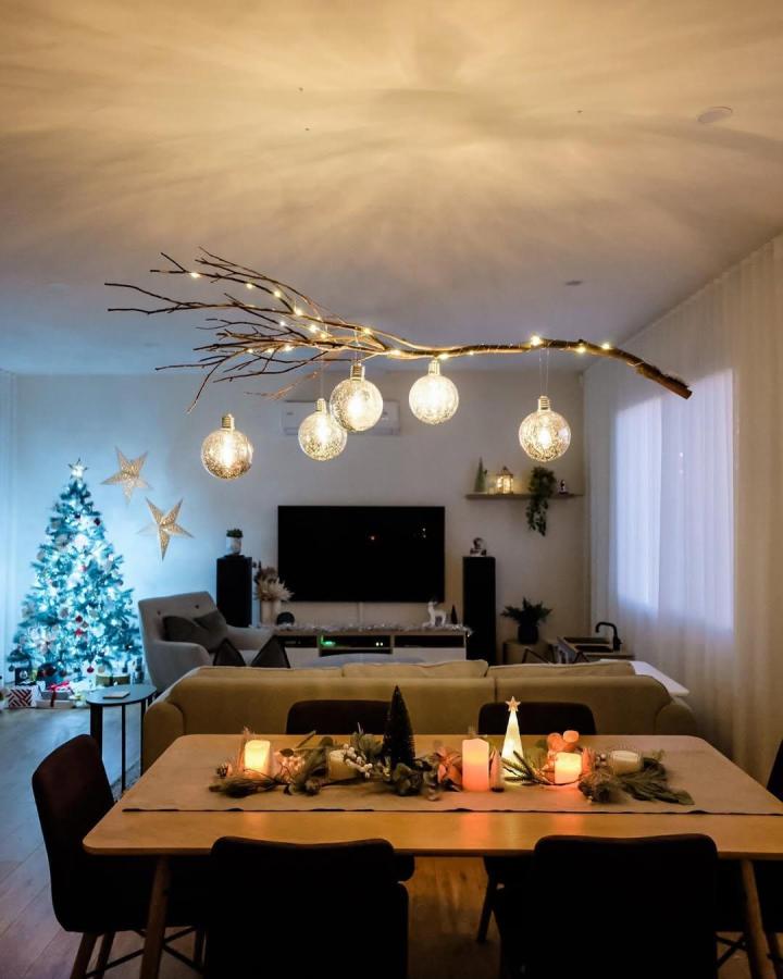 Warm white natural branch chandelier from @themorettons. Textured glass globes glow above a festive dining room.