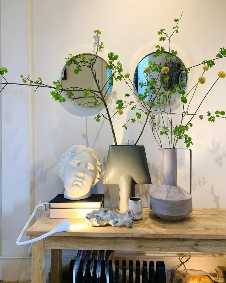 Green leafy branch arrangement from @gianluca.critelli. Yellow globes frame round mirrors above a console.