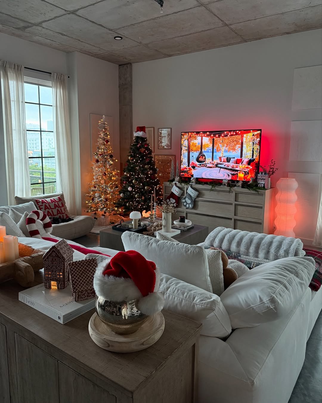 A cozy apartment living room with two decorated Christmas trees, stockings, glowing lights, and festive red accents