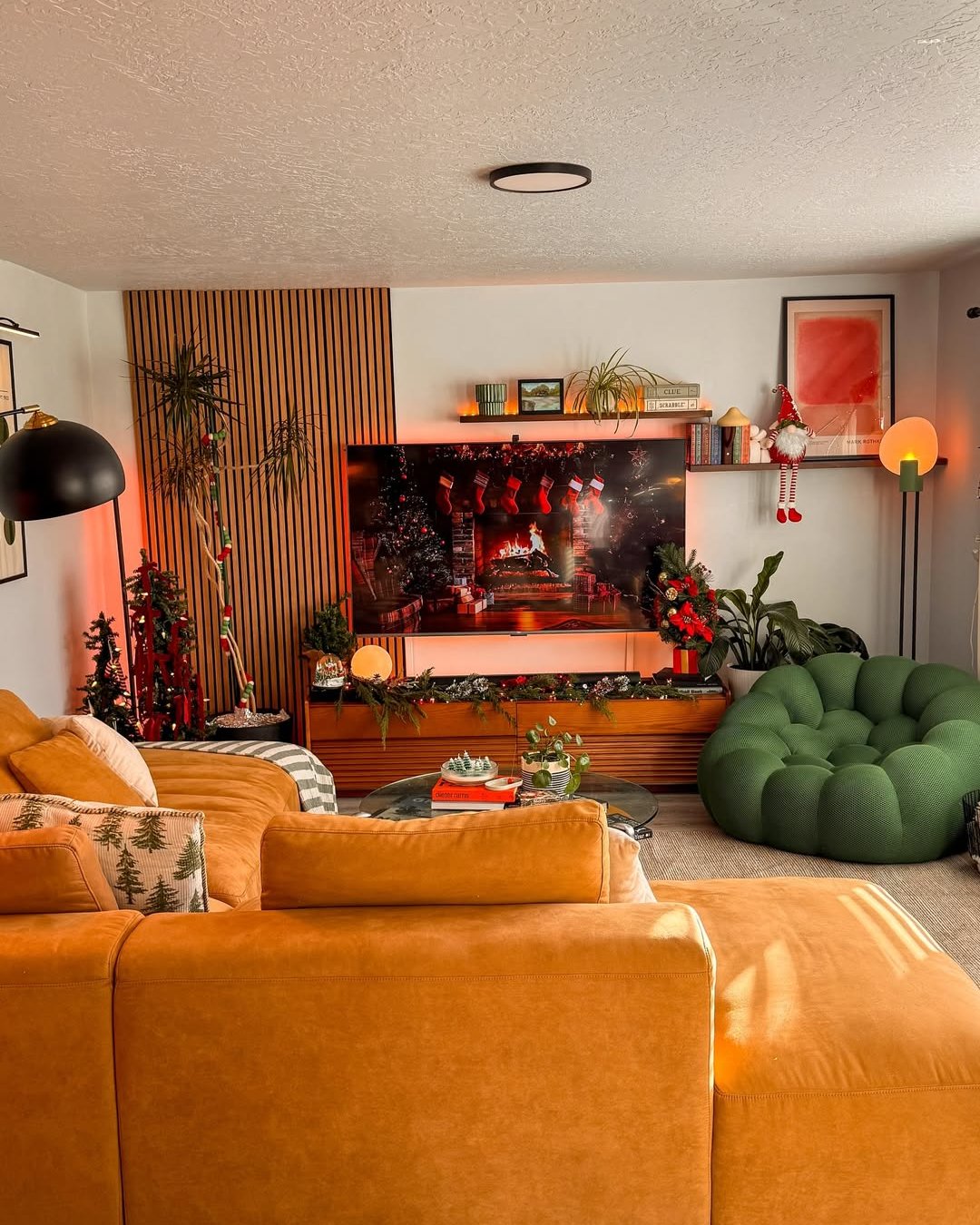 Cozy apartment holiday living room with a glowing TV fireplace, stockings, garland, and festive greenery