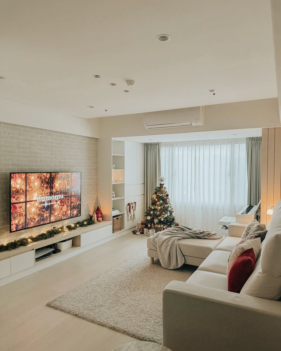 Cozy apartment living room with Christmas tree, garland lights, neutral furnishings, and festive red accents