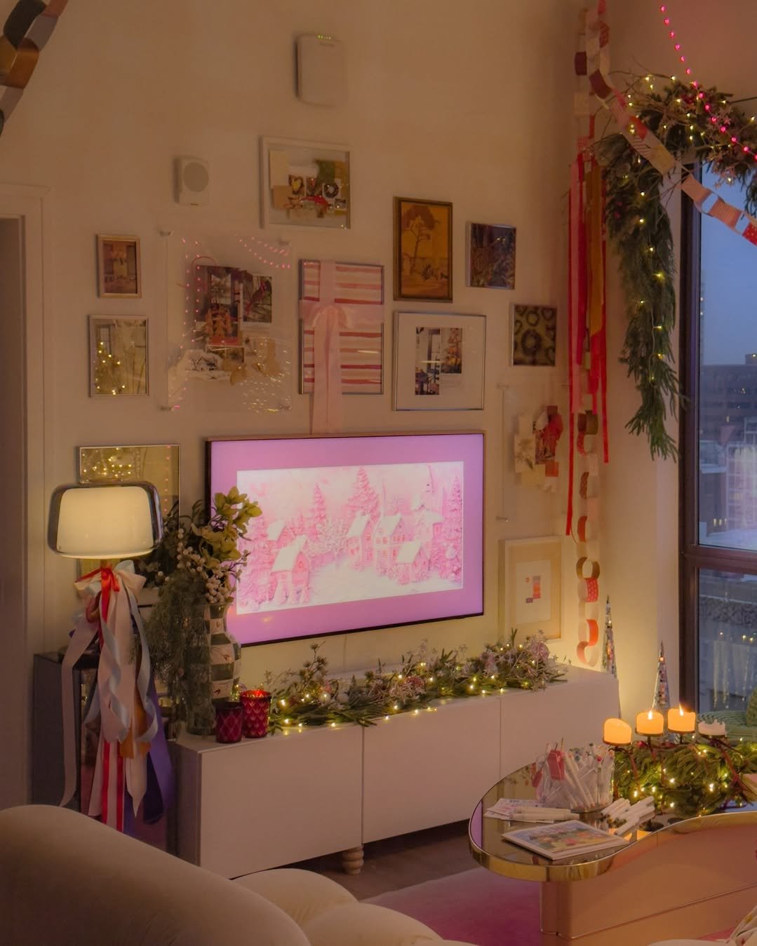 Festive apartment living room with ribbon garlands, glowing greenery, candles, and pink Christmas lighting