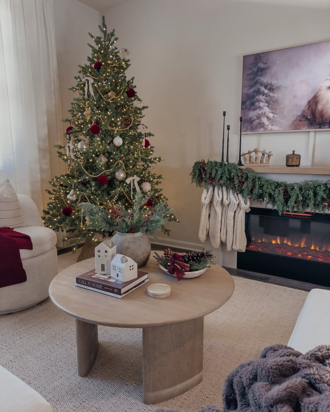 Warm apartment holiday living room with a decorated tree, evergreen mantel garland, stockings, and glowing fireplace
