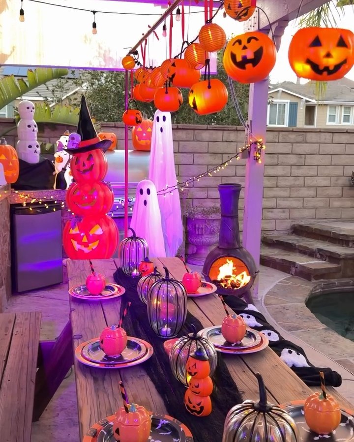 Orange pumpkin lanterns, glowing ghosts, and Halloween table decor create a festive outdoor party setting