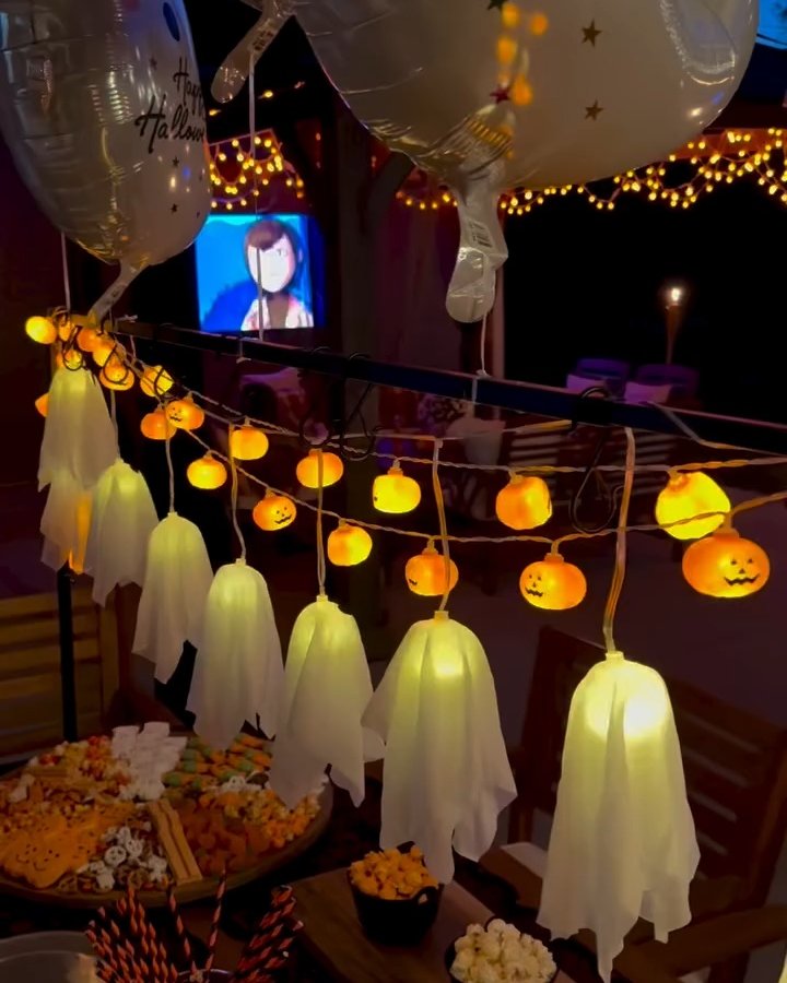 Glowing ghost lanterns and pumpkin lights decorate a festive outdoor Halloween gathering