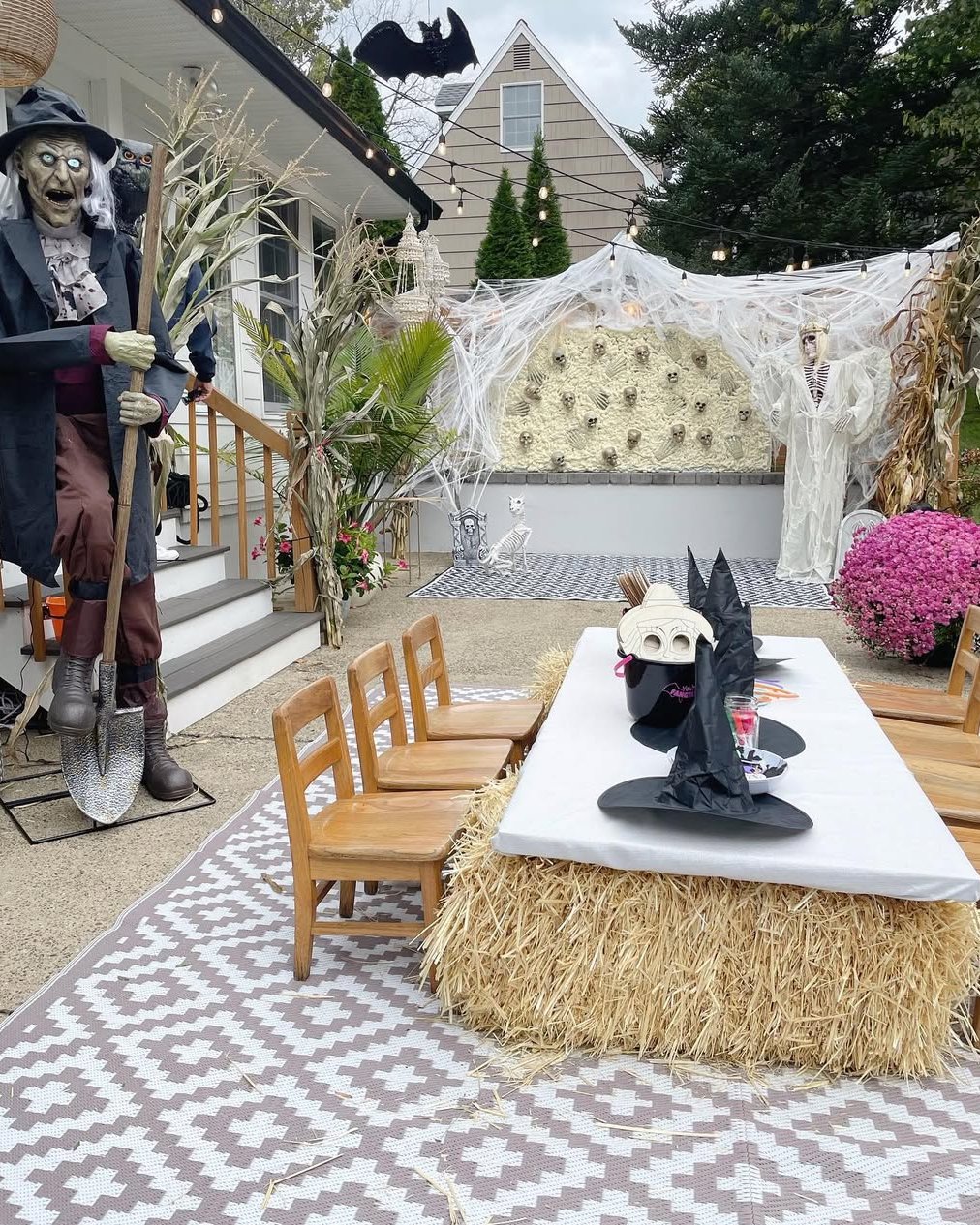 Spooky outdoor party with skull webbing, skeleton decor, hay bales, witch hats, and string lights