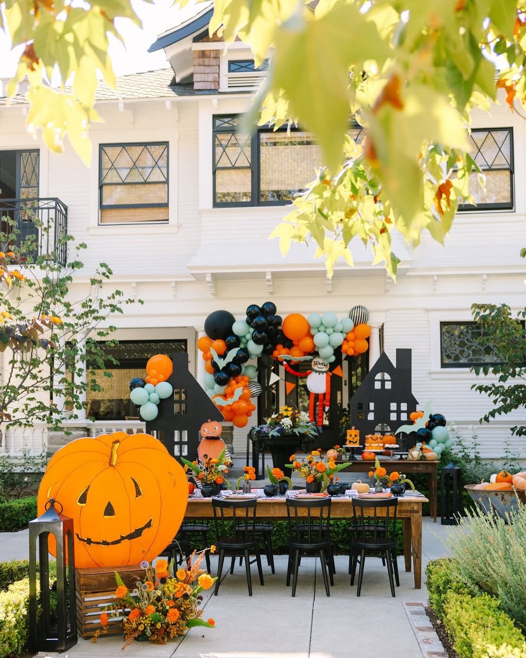 Colorful backyard Halloween dining table with oversized pumpkin decor, balloons, haunted houses, lanterns, and marigold arrangements