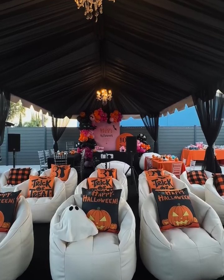 White lounge chairs with Halloween pillows beneath a black canopy create a cozy outdoor movie party setting