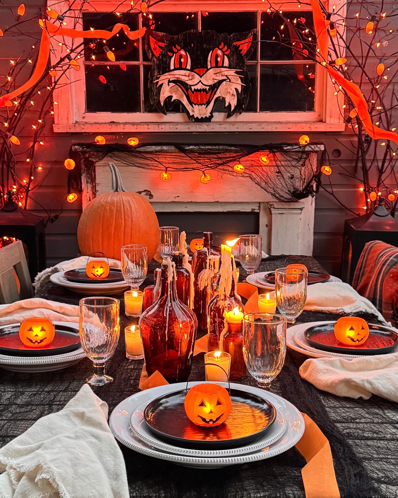 Pumpkin-lit outdoor Halloween table with black gauze, orange lights, candles, and spooky place settings