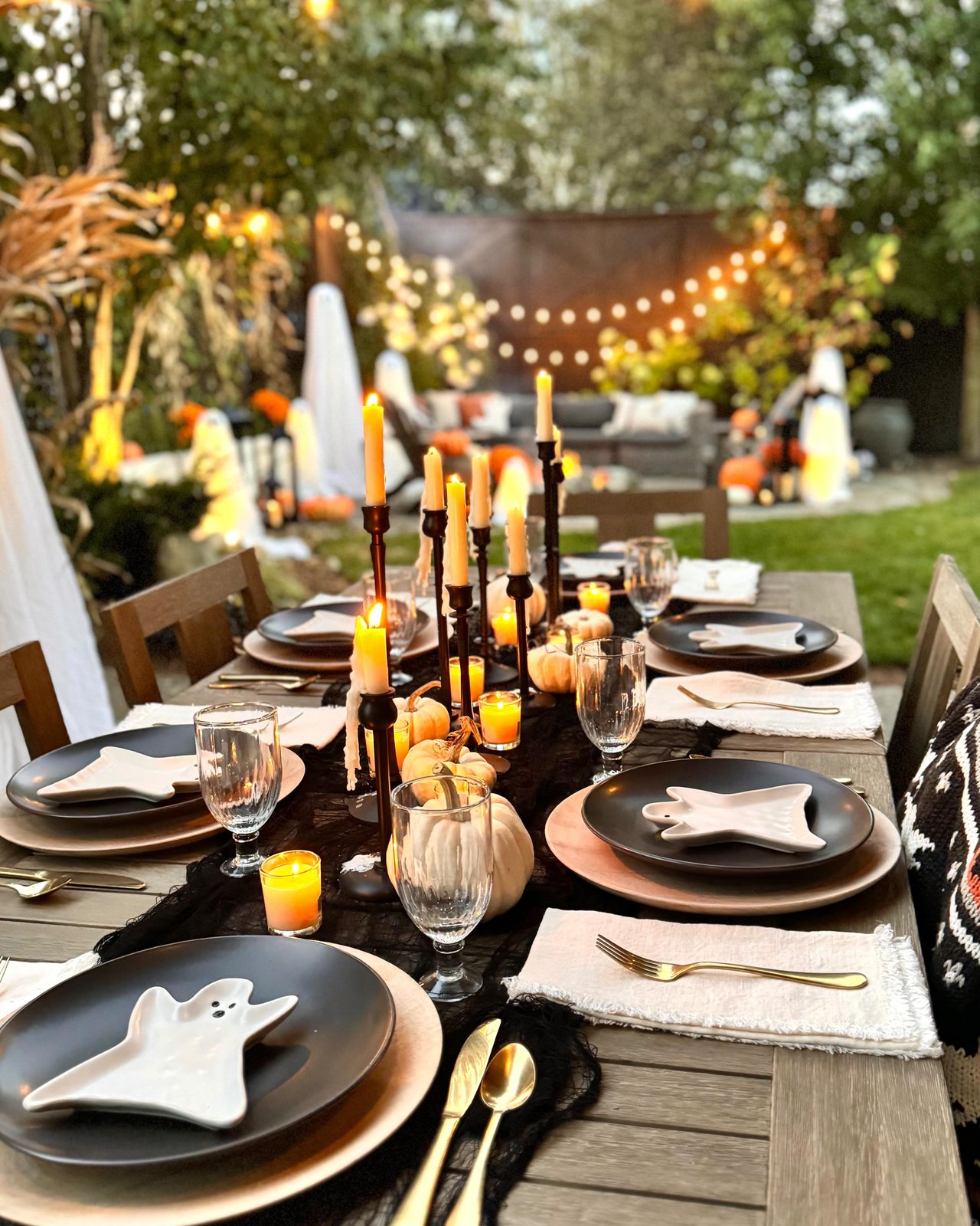 backyard halloween party ideas with ghost plates, pumpkins, black candles, and an elegant outdoor tablescape