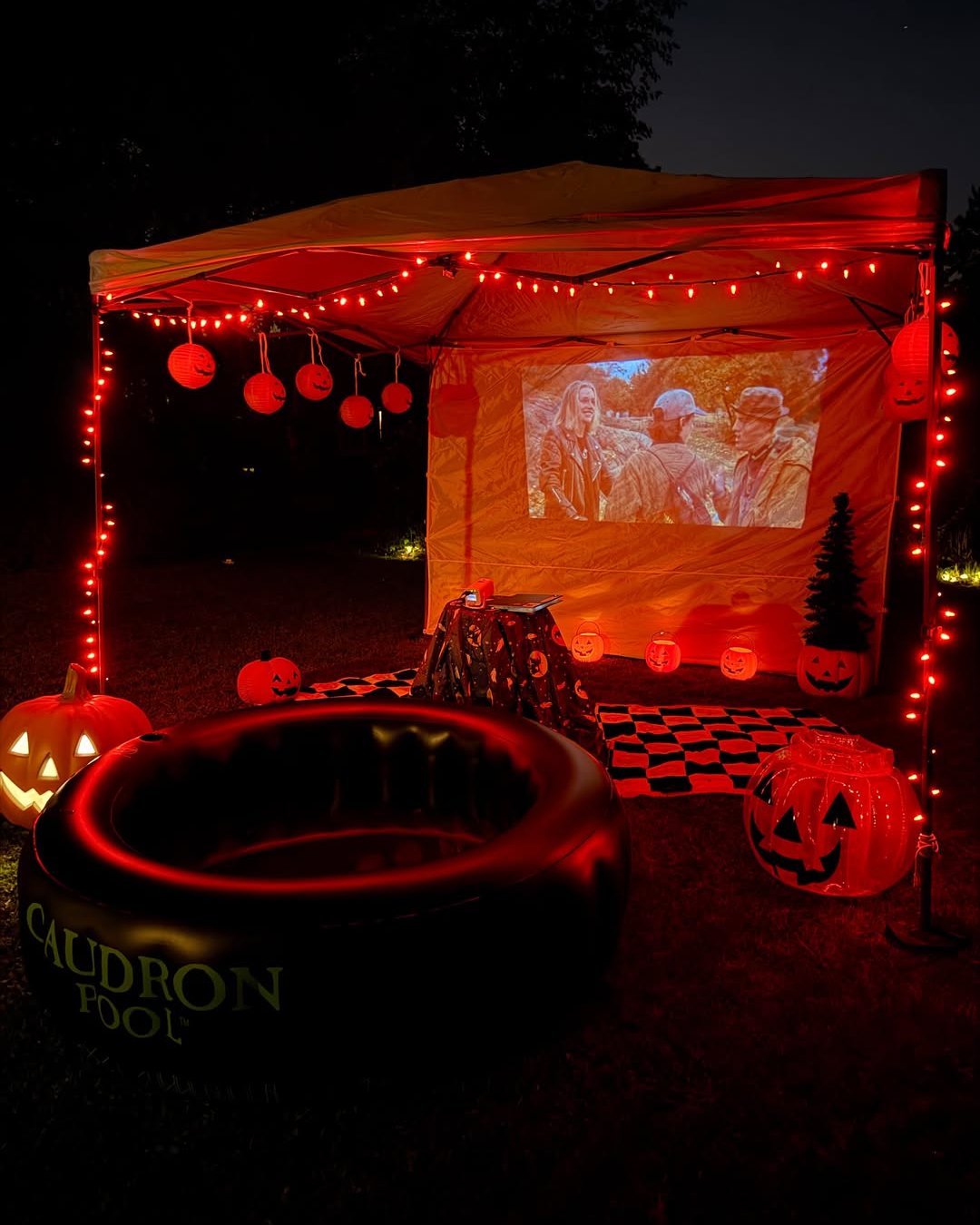 Glowing backyard Halloween movie setup with pumpkins, red lights, and an outdoor projection screen