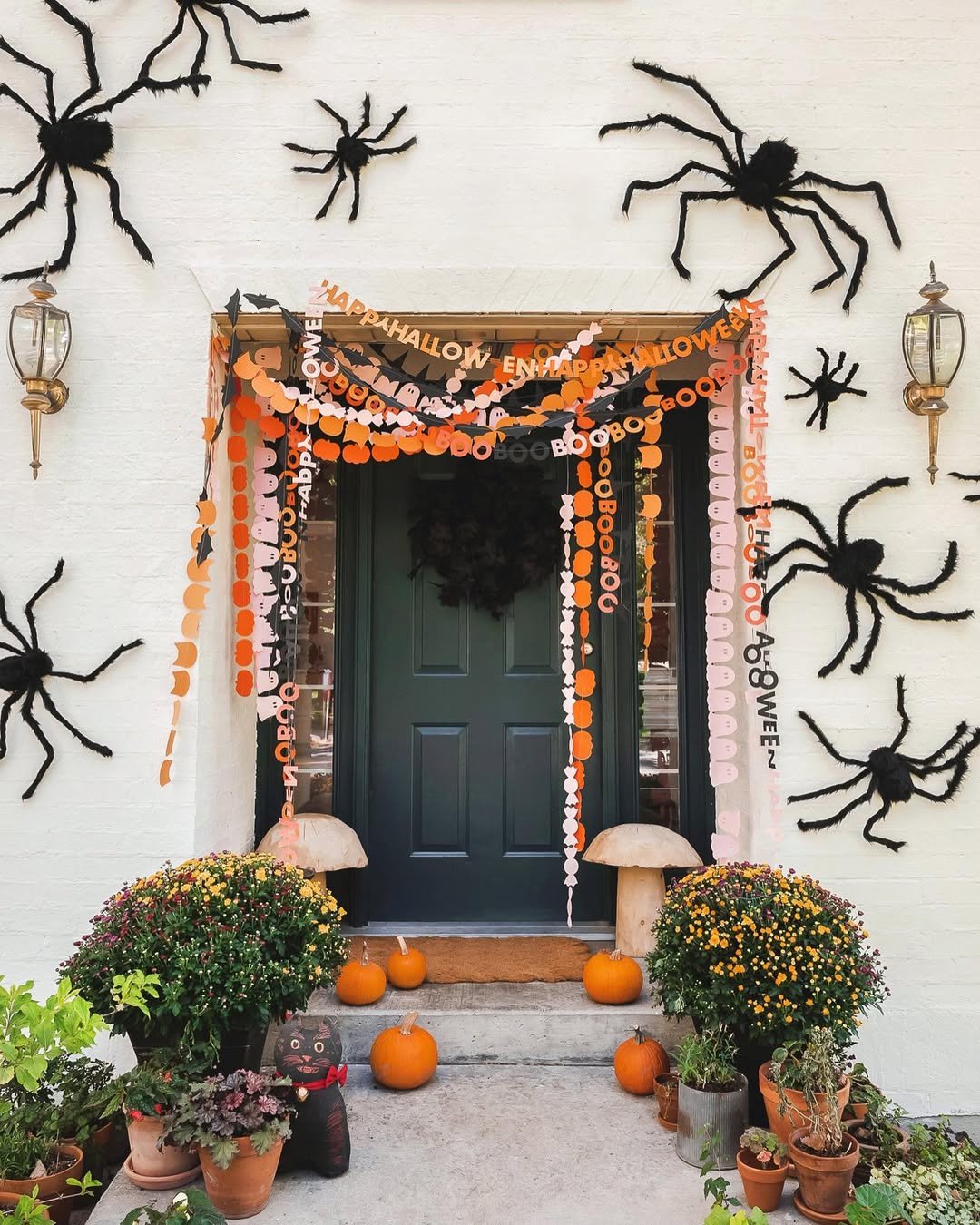 Spooky backyard party entrance with paper garlands, pumpkins, potted mums, and oversized black spiders