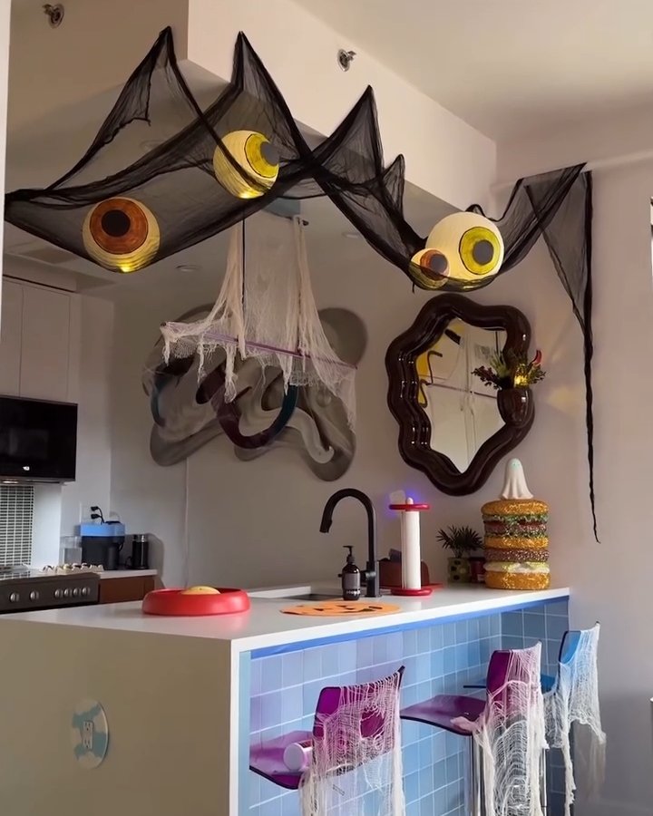 Black spiderweb ceiling decor with oversized glowing eyes in a Halloween party kitchen