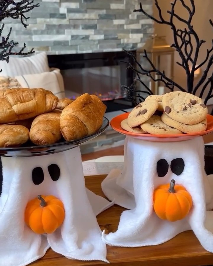 White ghost serving stands with pumpkins, pastries, cookies, and black branch decorations for a budget-friendly Halloween table