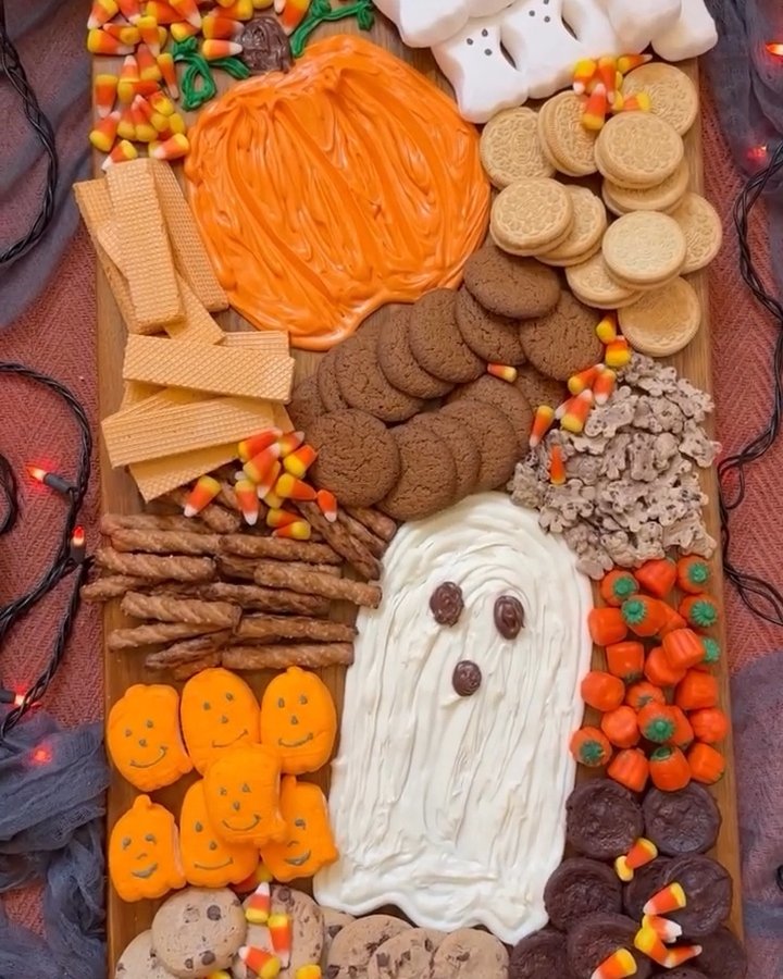 Halloween snack board with ghost dip, pumpkin treats, cookies, candy corn, and warm string lights