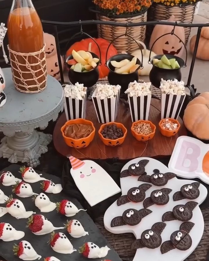 Festive Halloween snack table with pumpkin bowls, ghost treats, bat cookies, and striped popcorn containers