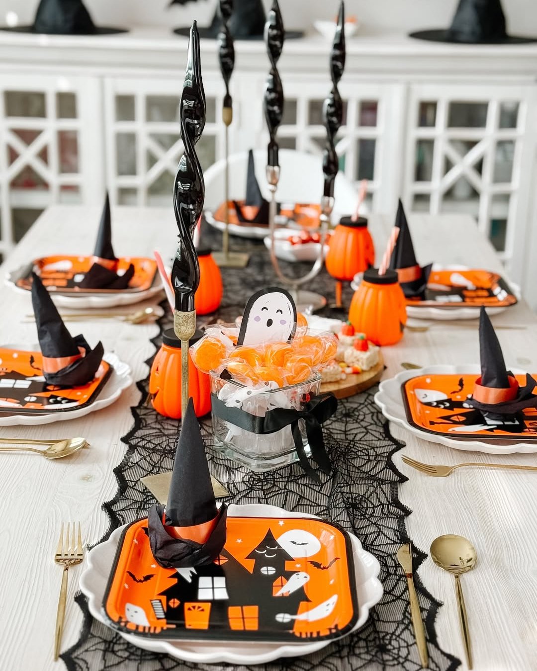 Halloween table decor with witch hat napkins, pumpkin cups, candy, and spooky orange place settings