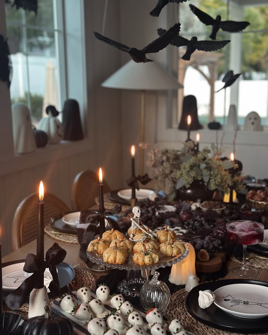 cheap halloween party ideas featuring a candlelit table with hanging black ravens, ghosts, pumpkins, and spooky treats