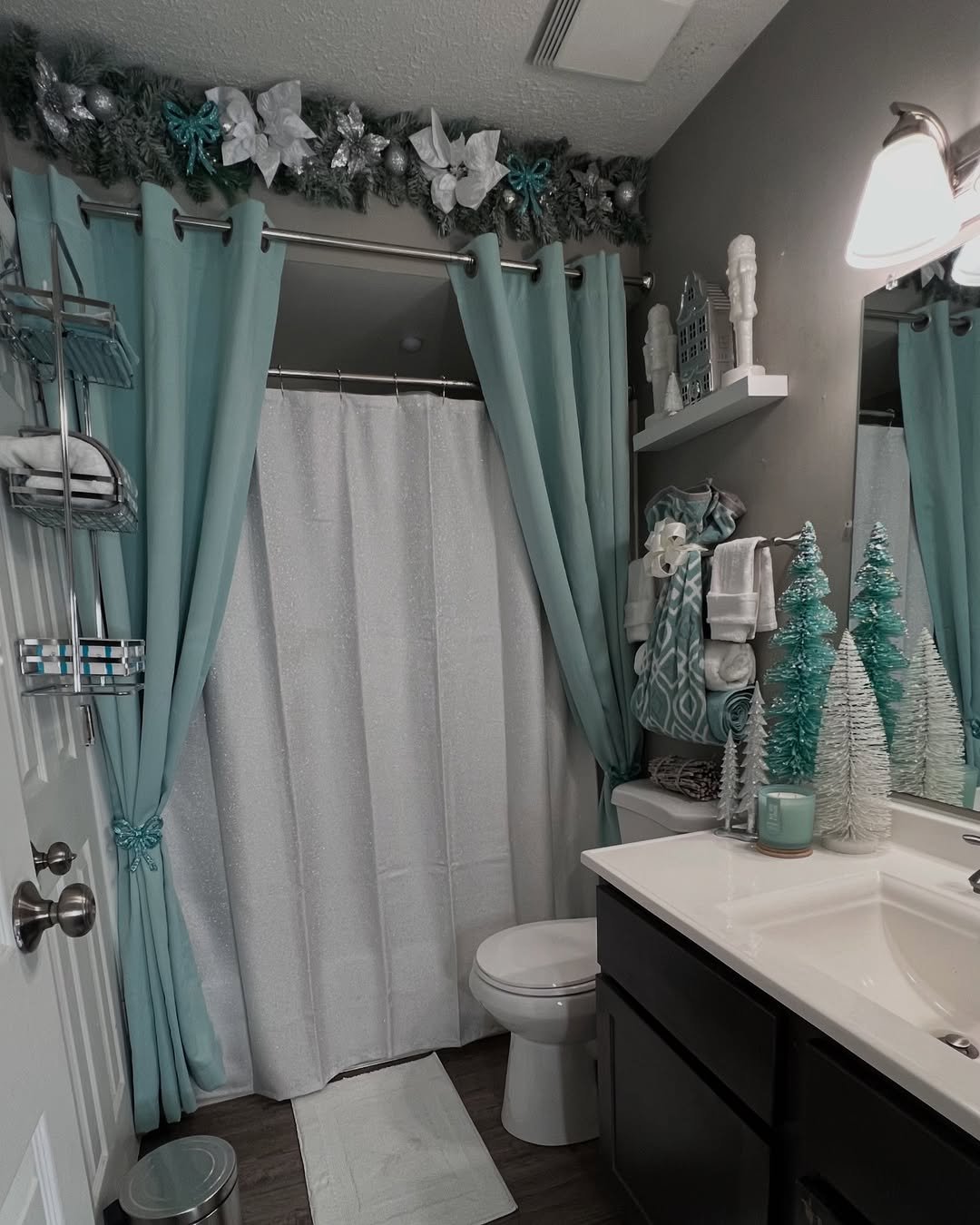 Teal and white Christmas bathroom with garland, bottlebrush trees, aqua curtains, and sparkling seasonal accents