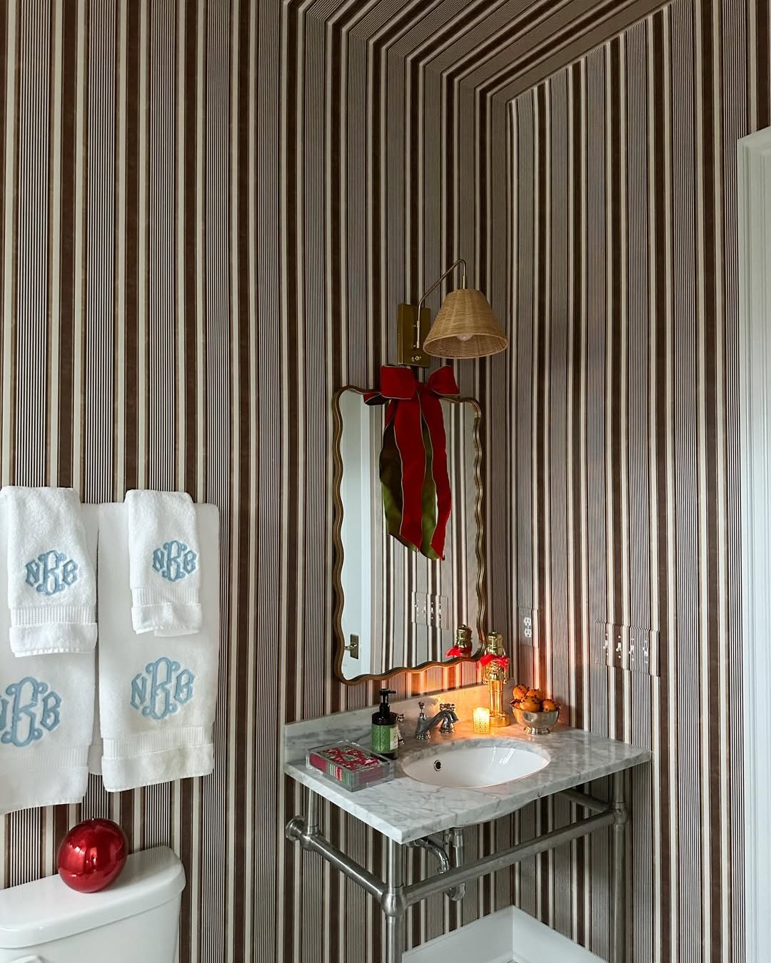 Striped bathroom with a red bow, festive ornament, marble vanity, and monogrammed towels